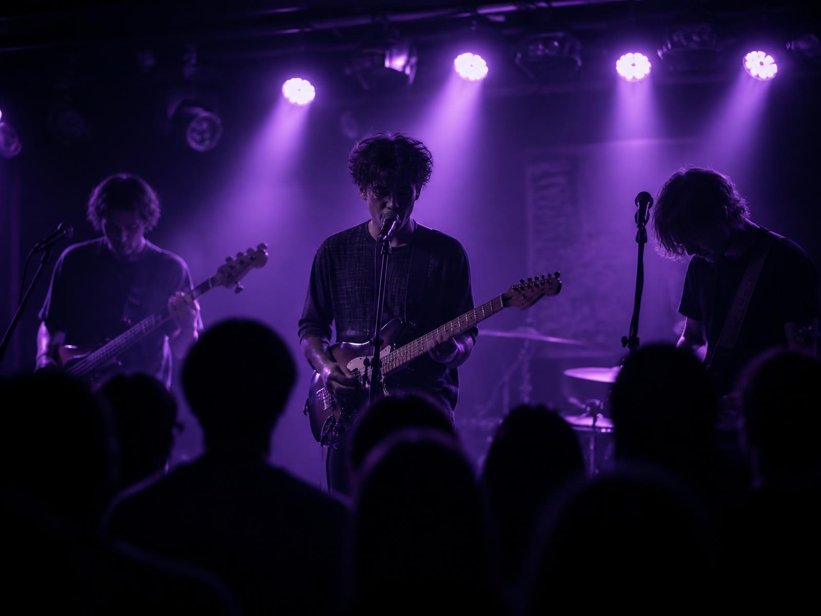 An emerging band playing a packed small venue lit in purple and lilac